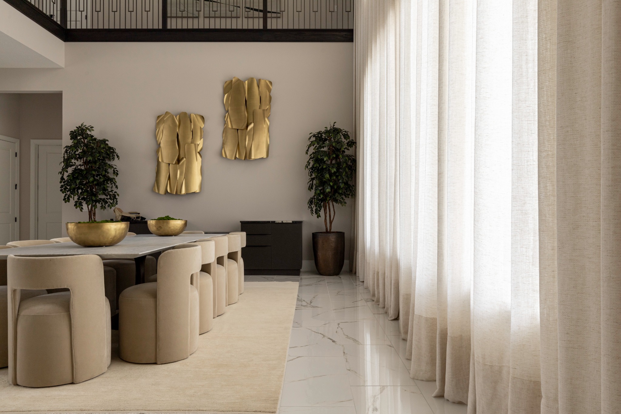 Floor-to-ceiling sheer curtains beside a dining room with ivory chairs and gold wall sculptures